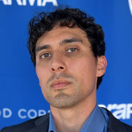 A man with short black curly hair looking at the camera