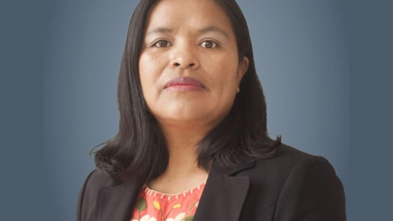 Headshot of a poised woman in black blazer and floral blouse against blue-gray background