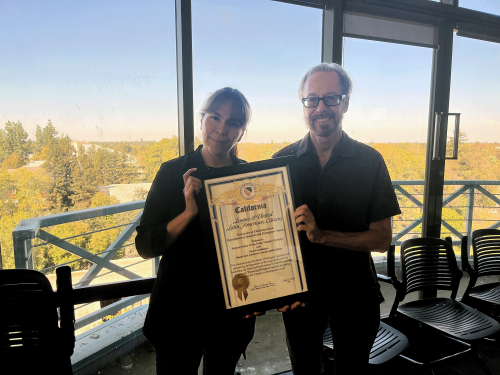 A man and a woman stand holding a framed award