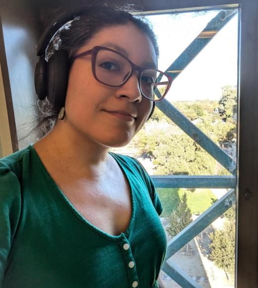 A woman wearing classes stand by a window. She has a pair of headphones over her ears.