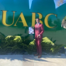 A man wearing a maroon suit in front of the letters UABC