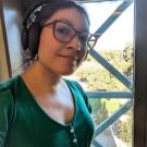 A woman wearing classes stand by a window. She has a pair of headphones over her ears.