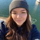 A woman wearing a beanie near a boat in the water