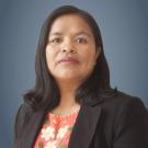 Headshot of a poised woman in black blazer and floral blouse against blue-gray background